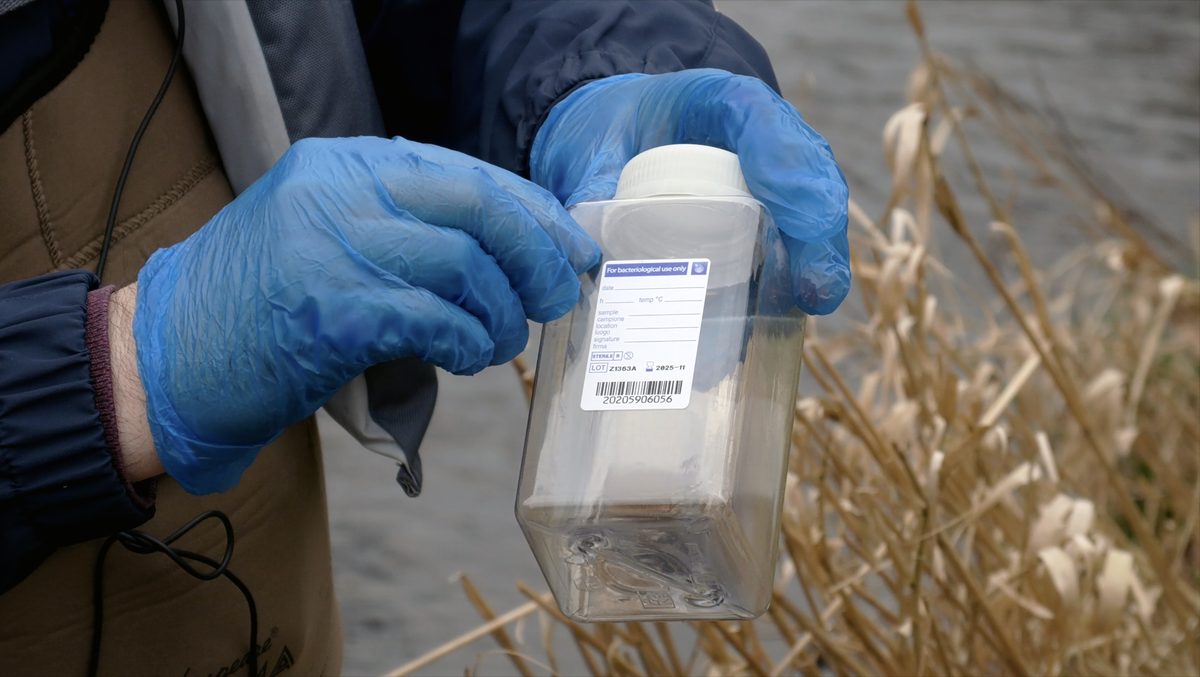 A surveyor sealing a labelled water sample bottle beside a river